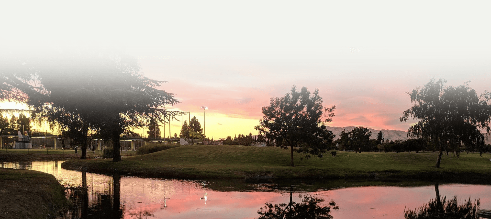 A scenic sunset view over a pond and course grounds with silhouetted trees and distant mountains.